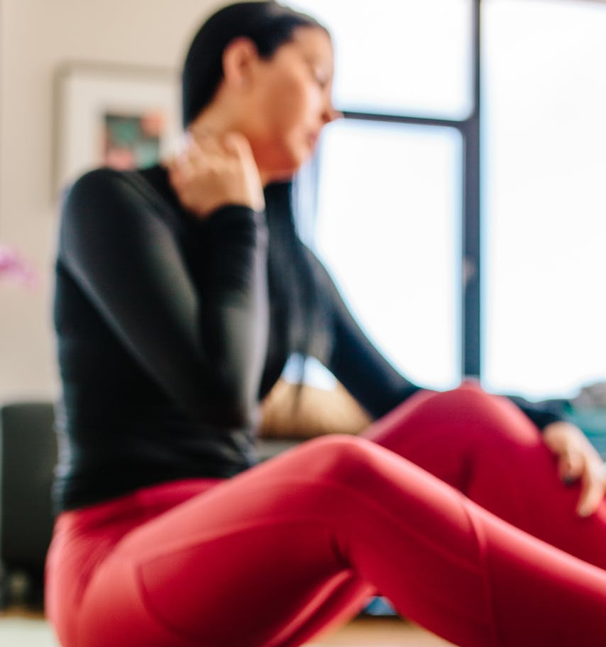 a blurry image of a person sitting on the floor holding a hand to their neck