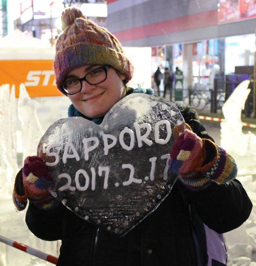 A photo of Sara in winter gear at the Sapporo Snow Festival holding a heart made out of ice that says, "Sapporo 2017.2.11".