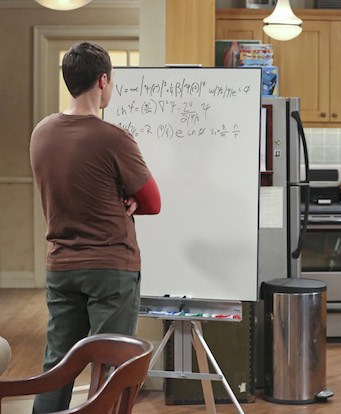 Sheldon Cooper from The Big Band Theory standing with his back to the camera, doing highly complicated math at his whiteboard.