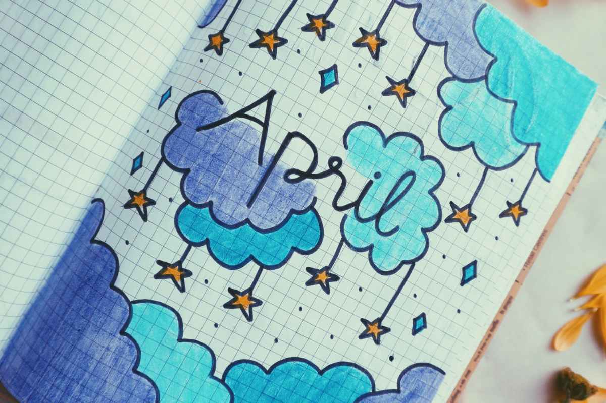 A photo of a drawn image in a notebook that reads "April" surrounded by blue and navy clouds with stars hanging from them.