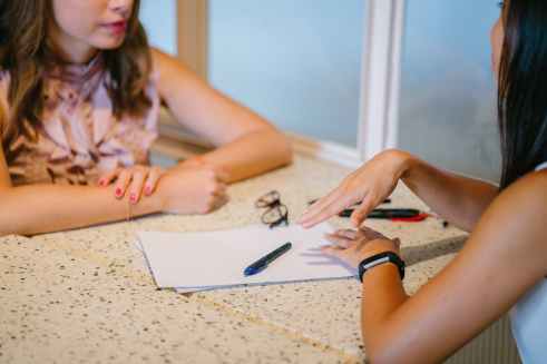 A photo showing two people sitting at a table, having a discussion. There is paper and pen in front of them, and one person is actively listening to the other.